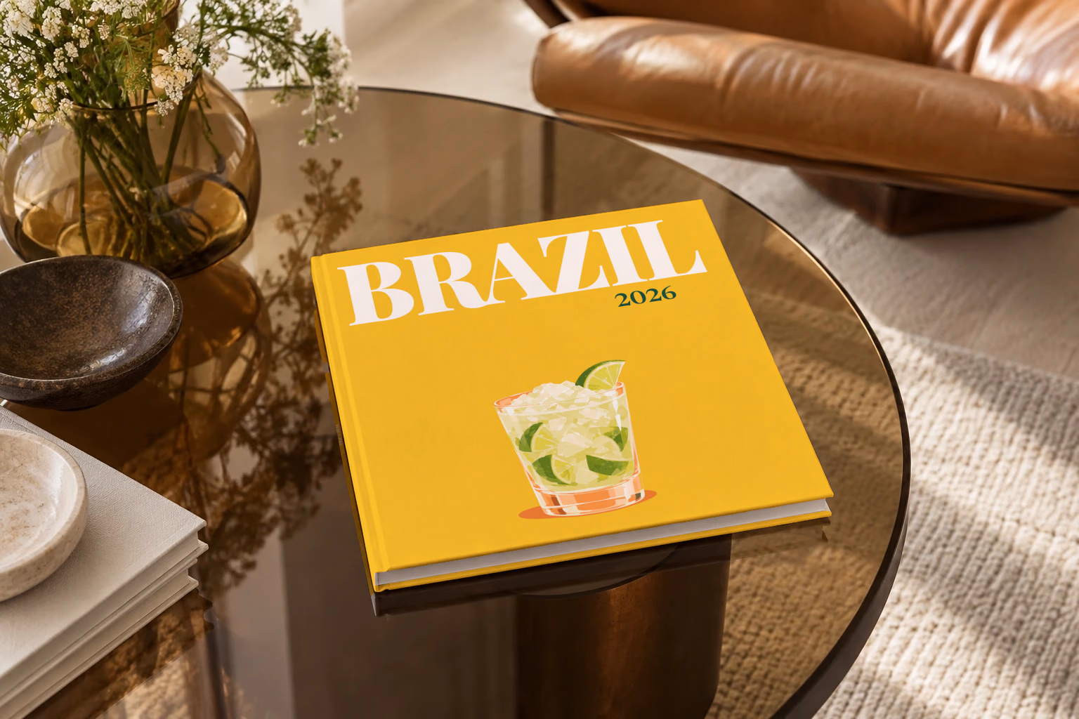 Brazil square hardcover photo book with the illustrated cover of a caipirinha with crushed ice and lime on golden yellow, on a smoked glass coffee table beside a leather armchair in warm afternoon light