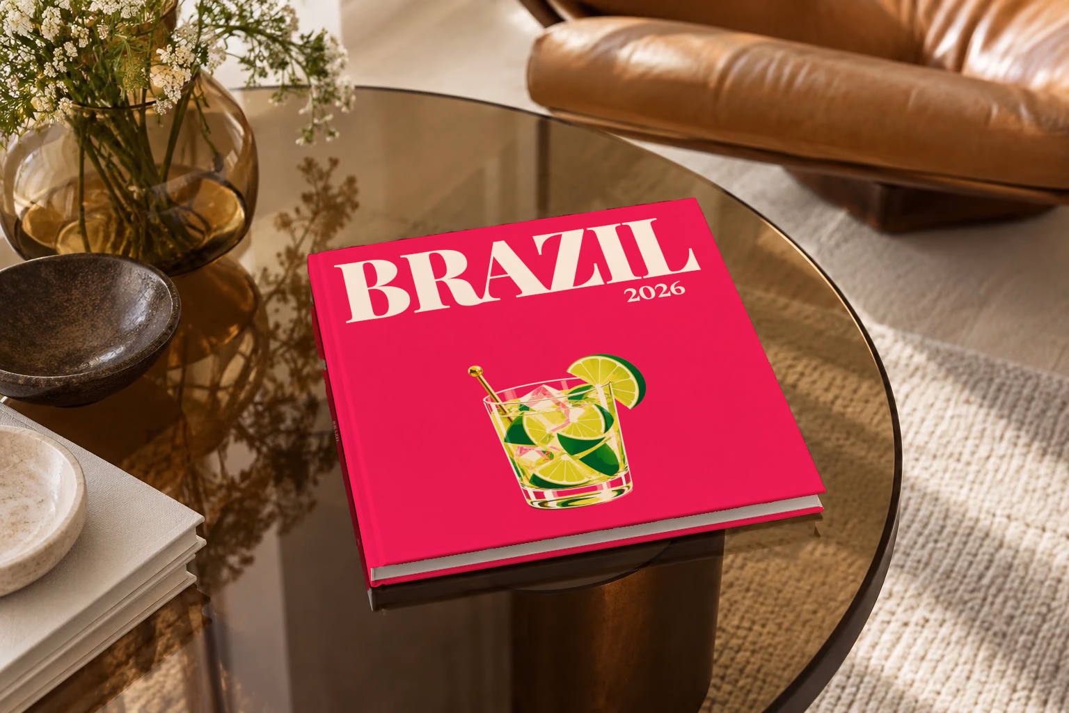 Brazil square hardcover photo book with the illustrated cover of a caipirinha with lime wedges on magenta, on a smoked glass coffee table beside a leather armchair in warm afternoon light