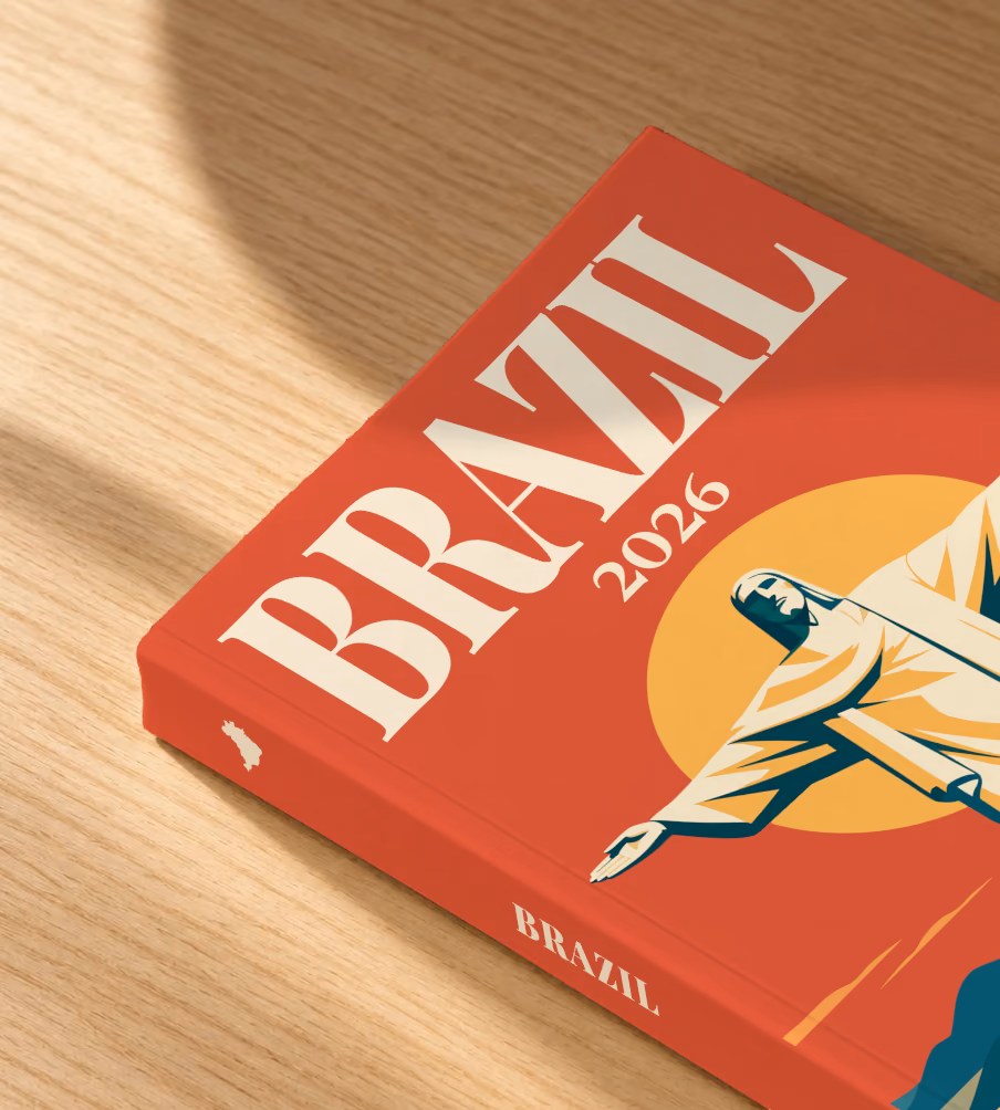 Brazil softcover photo book with the illustrated cover of Christ the Redeemer above Rio de Janeiro's bay at sunset on red-orange, lying on an oak desk in dappled afternoon sunlight