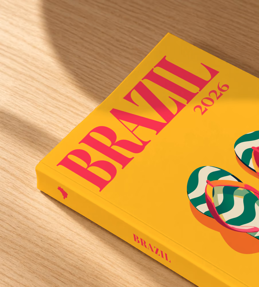 Brazil softcover photo book with the illustrated cover of a pair of flip-flops in Copacabana's wave pattern on yellow, lying on an oak desk in dappled afternoon sunlight