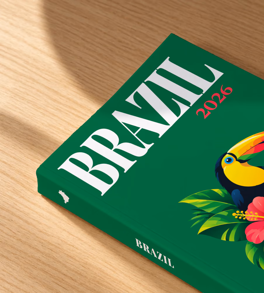 Brazil softcover photo book with the illustrated cover of a toucan among tropical leaves and a pink hibiscus on emerald green, lying on an oak desk in dappled afternoon sunlight