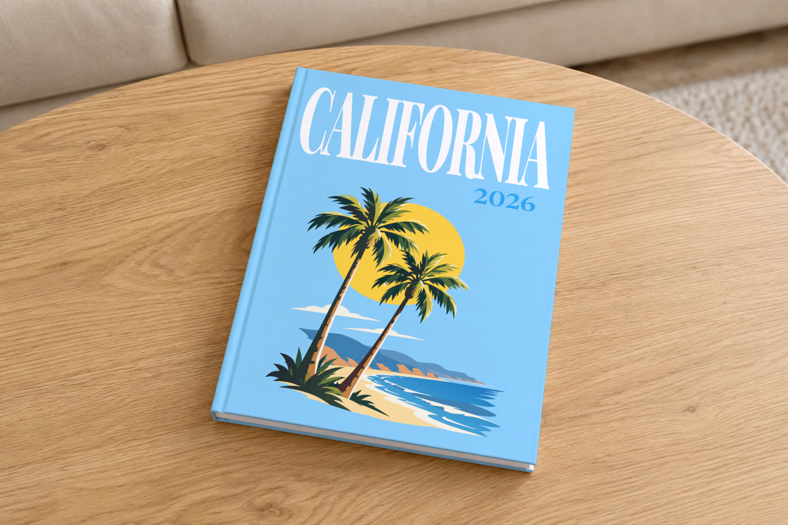 California hardcover photo book with the illustrated cover of palm trees and a beach under a yellow sun on sky blue, on a round oak coffee table in a bright living room