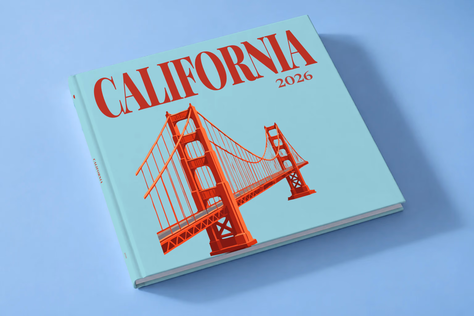 California square hardcover photo book with the illustrated cover of the Golden Gate Bridge on pale aqua, lying on a pale blue studio backdrop