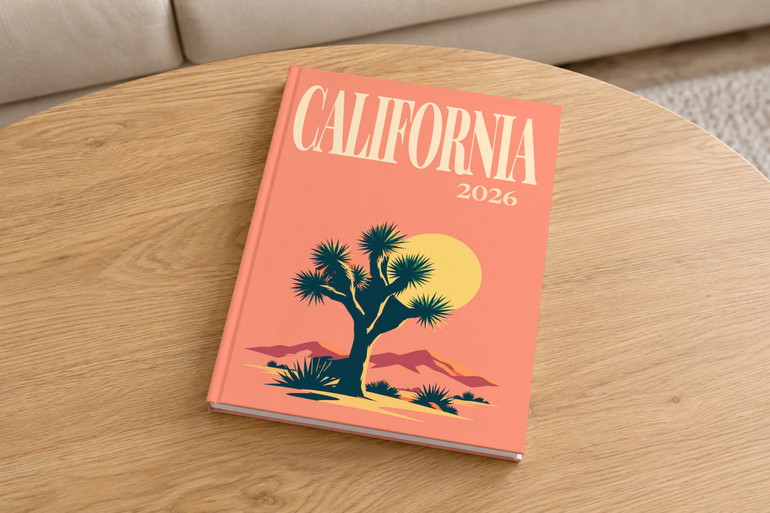 California hardcover photo book with the illustrated cover of a Joshua tree and desert hills under a low sun on coral, on a round oak coffee table in a bright living room