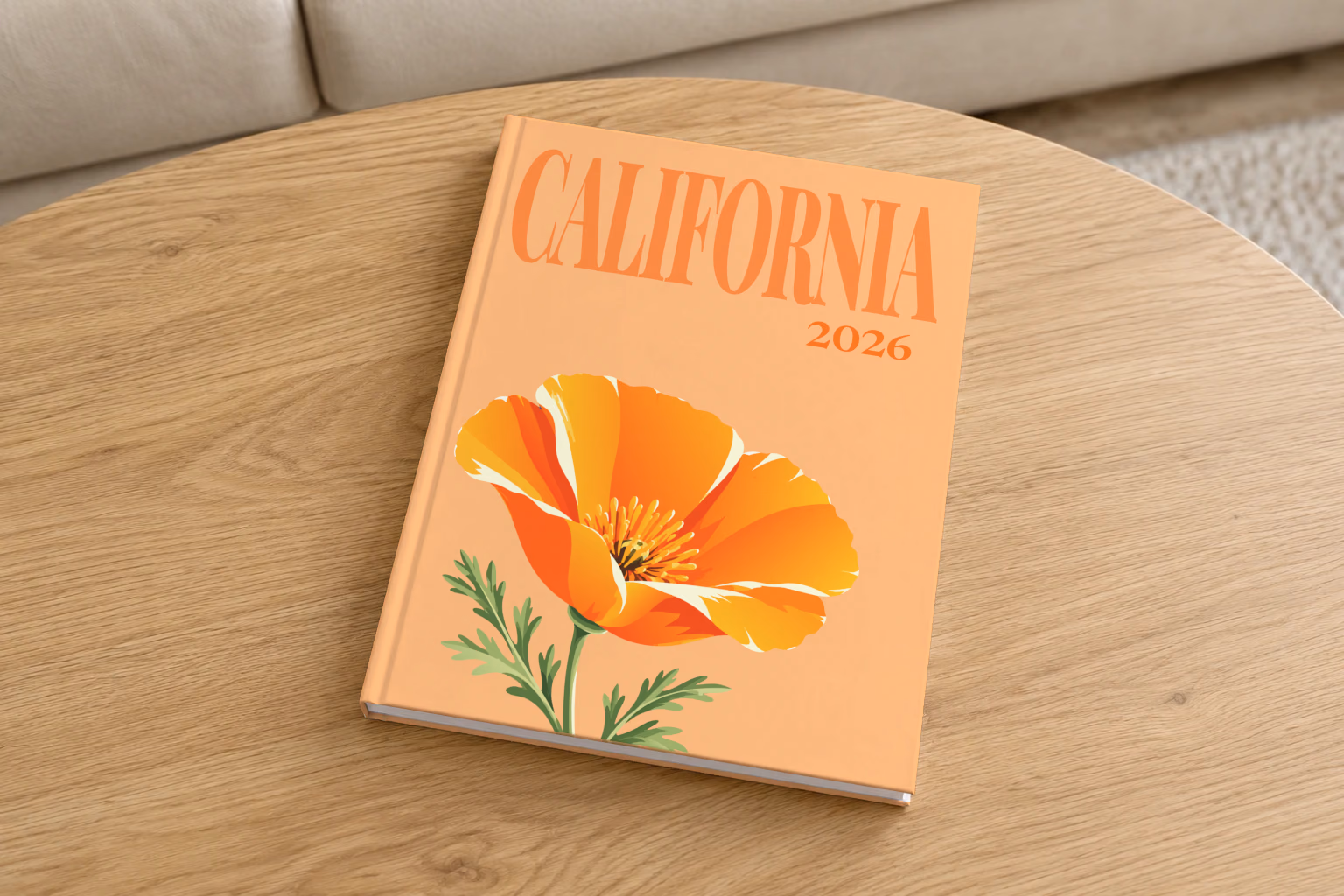 California hardcover photo book with the illustrated cover of a California poppy on peach, on a round oak coffee table in a bright living room