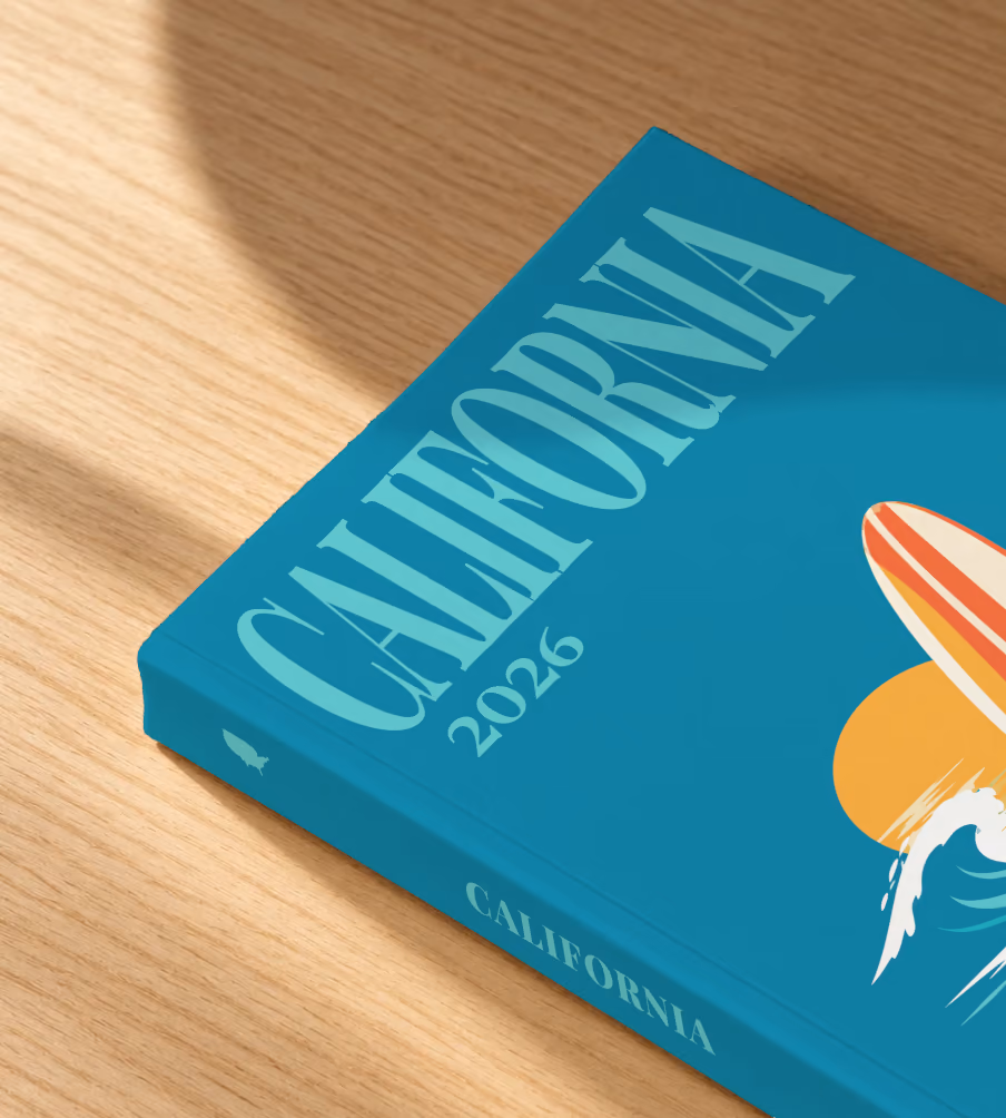 California softcover photo book with the illustrated cover of a surfboard, a wave and the sun on teal, lying on an oak desk in dappled afternoon sunlight