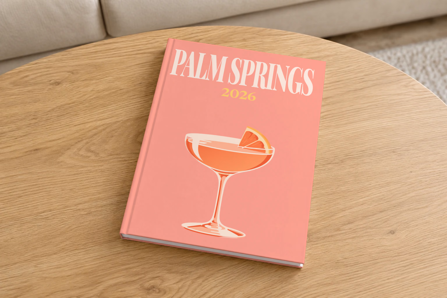 California hardcover photo book with the Palm Springs illustrated cover of a coupe cocktail with grapefruit on salmon pink, on a round oak coffee table in a bright living room
