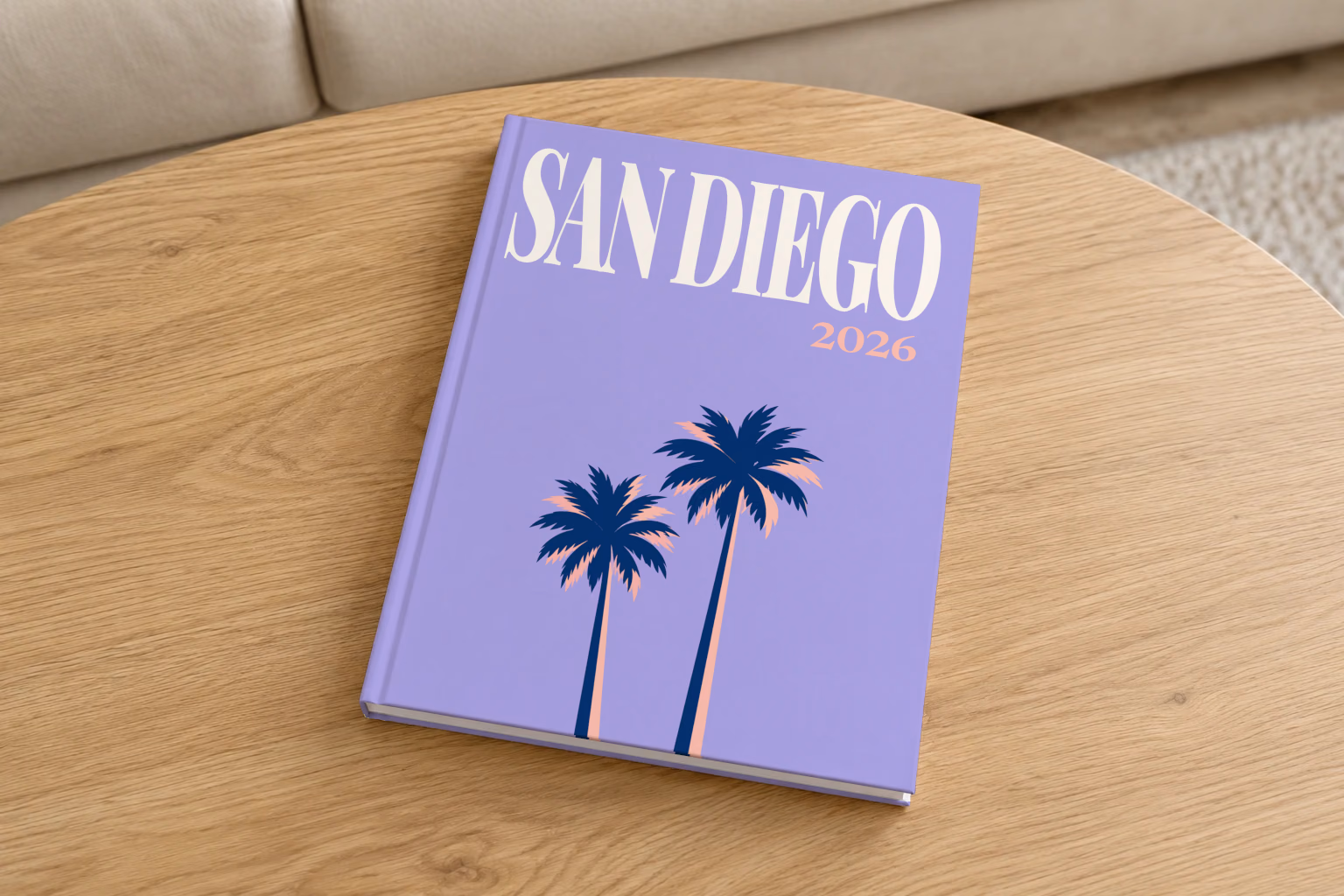 California hardcover photo book with the San Diego illustrated cover of palm trees on lilac, on a round oak coffee table in a bright living room