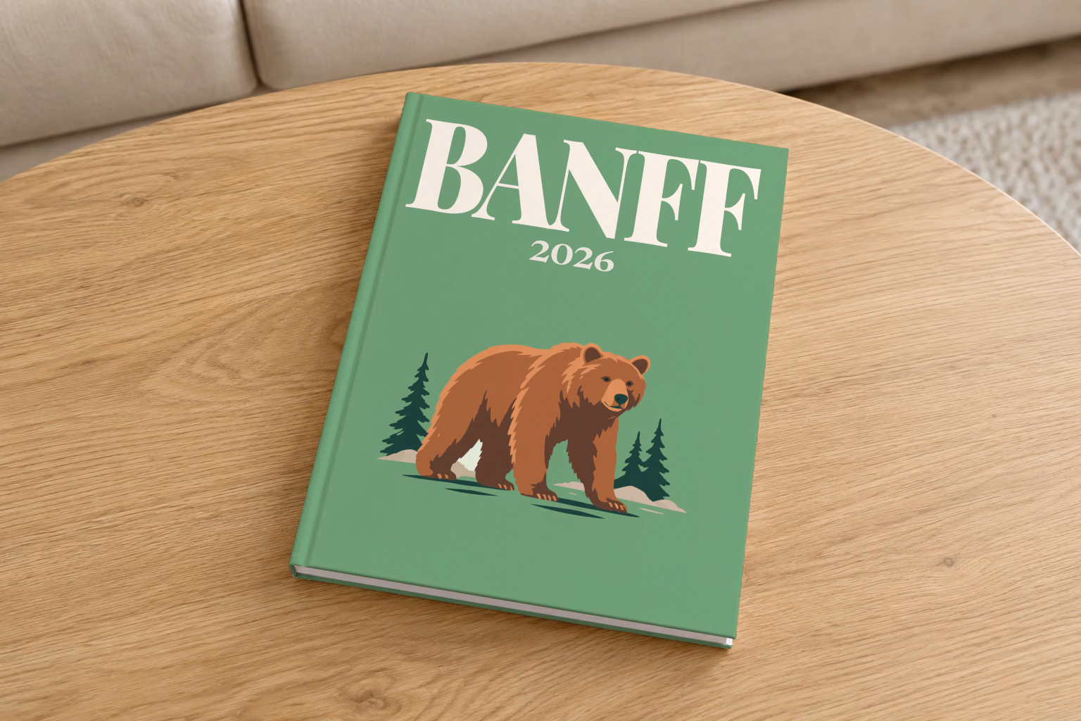 Canada hardcover photo book with the Banff illustrated cover of a grizzly bear and pines on sage green, on a round oak coffee table in a bright living room