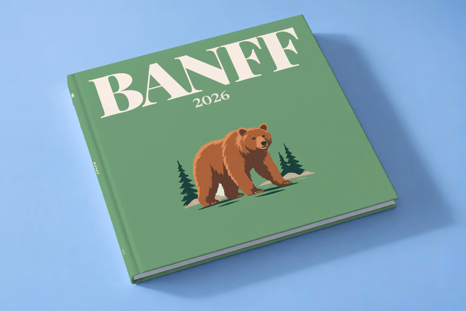 Canada square hardcover photo book with the Banff illustrated cover of a grizzly bear and pines on sage green, lying on a pale blue studio backdrop