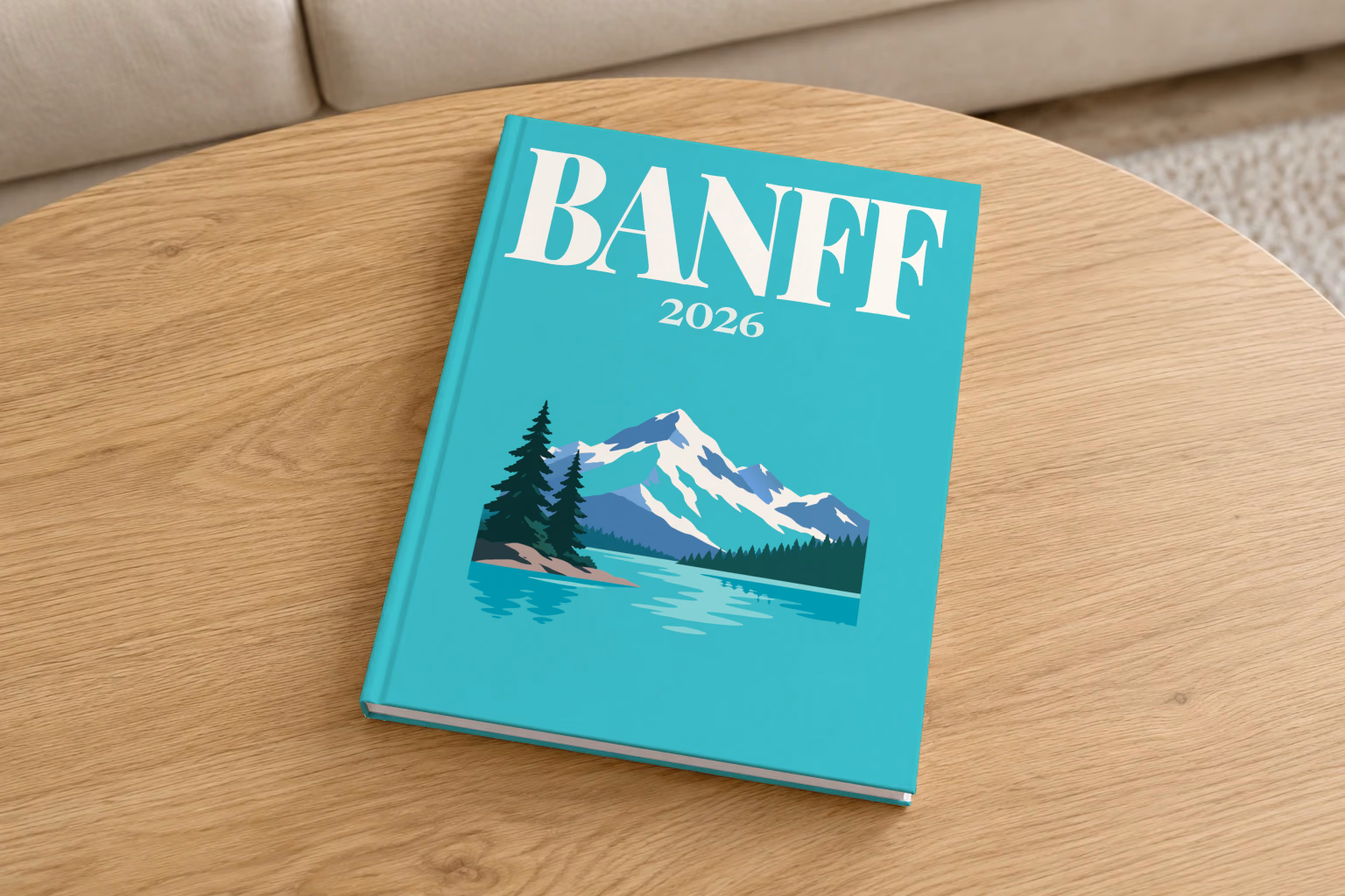 Canada hardcover photo book with the Banff illustrated cover of a mountain lake, snowy peaks and pines on turquoise, on a round oak coffee table in a bright living room