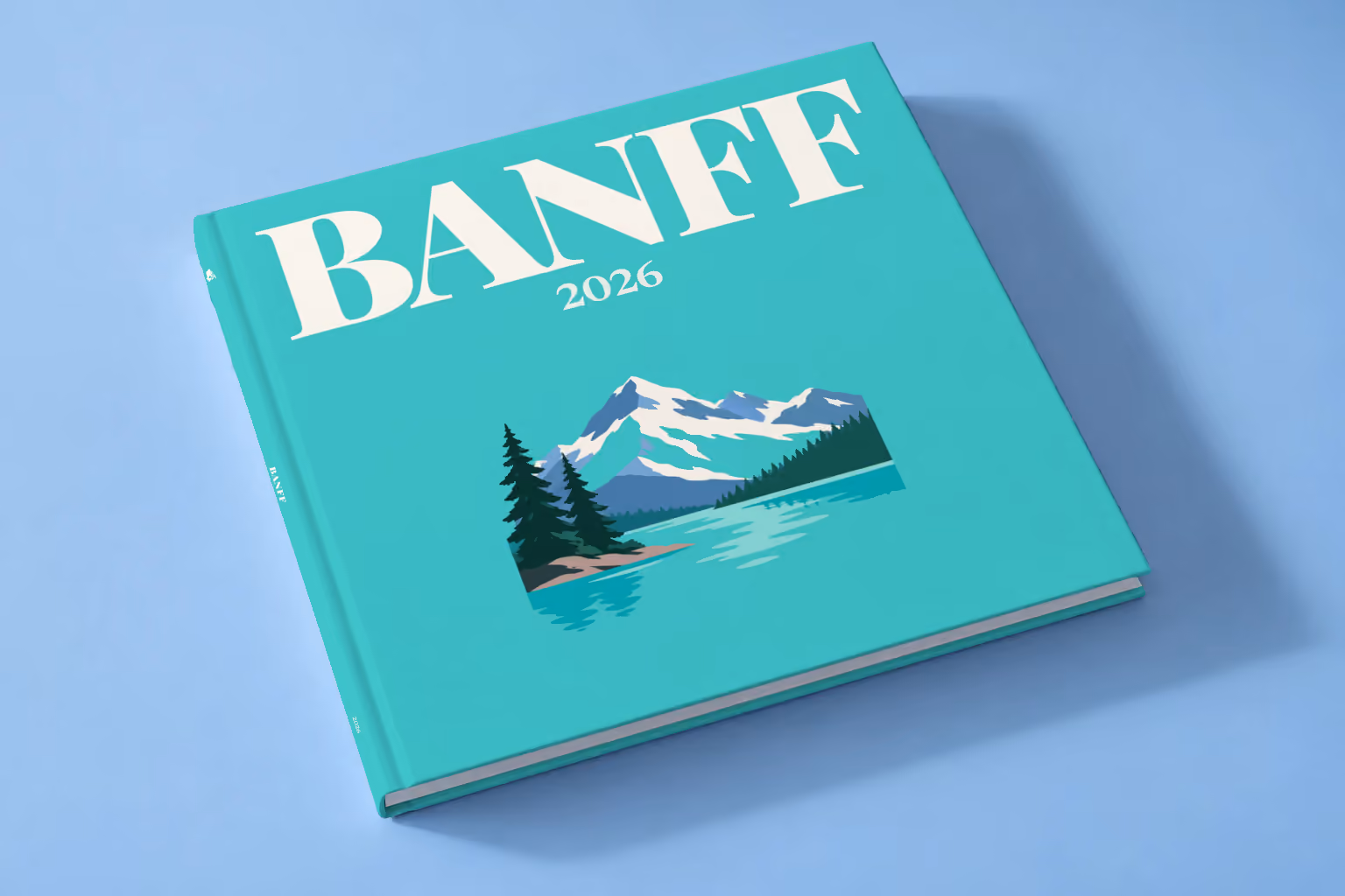 Canada square hardcover photo book with the Banff illustrated cover of a mountain lake, snowy peaks and pines on turquoise, lying on a pale blue studio backdrop