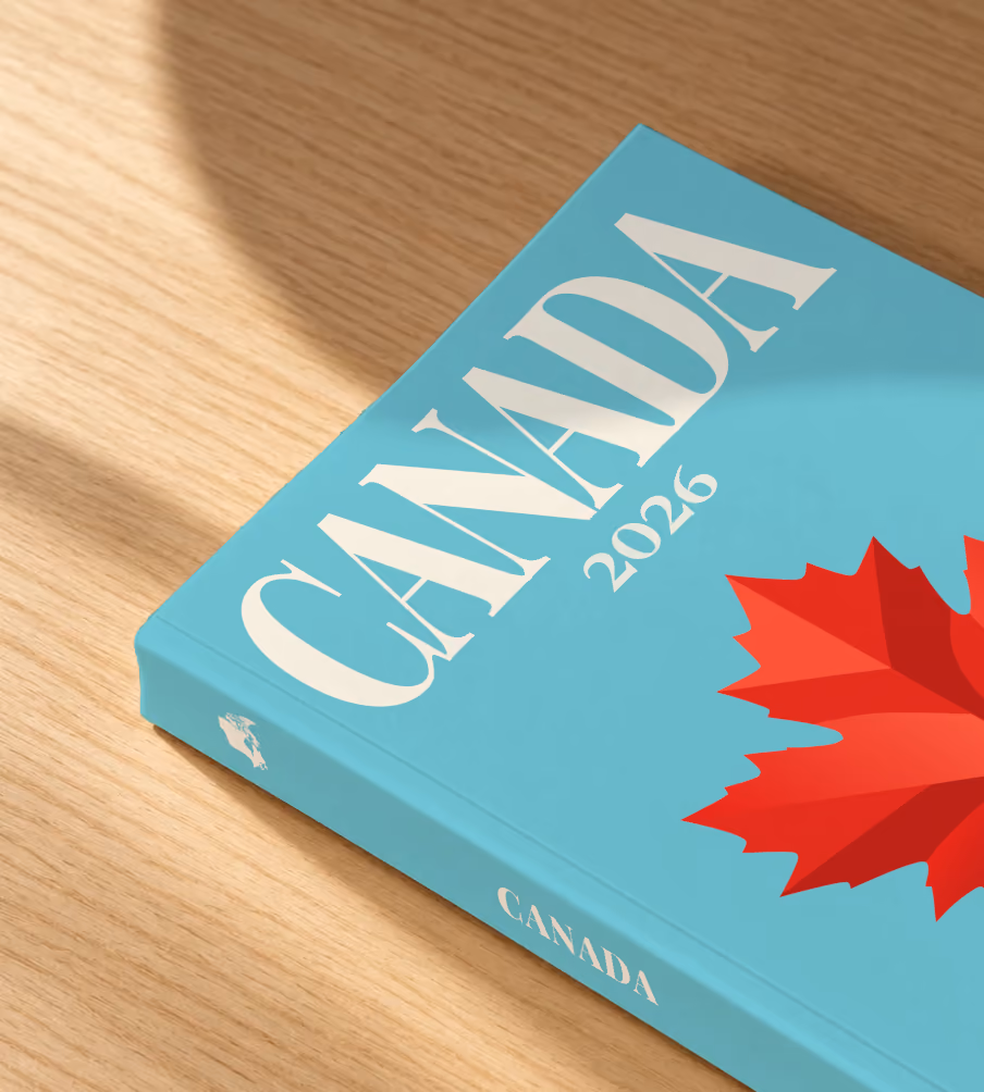 Canada softcover photo book with the illustrated cover of a red maple leaf on turquoise, lying on an oak desk in dappled afternoon sunlight