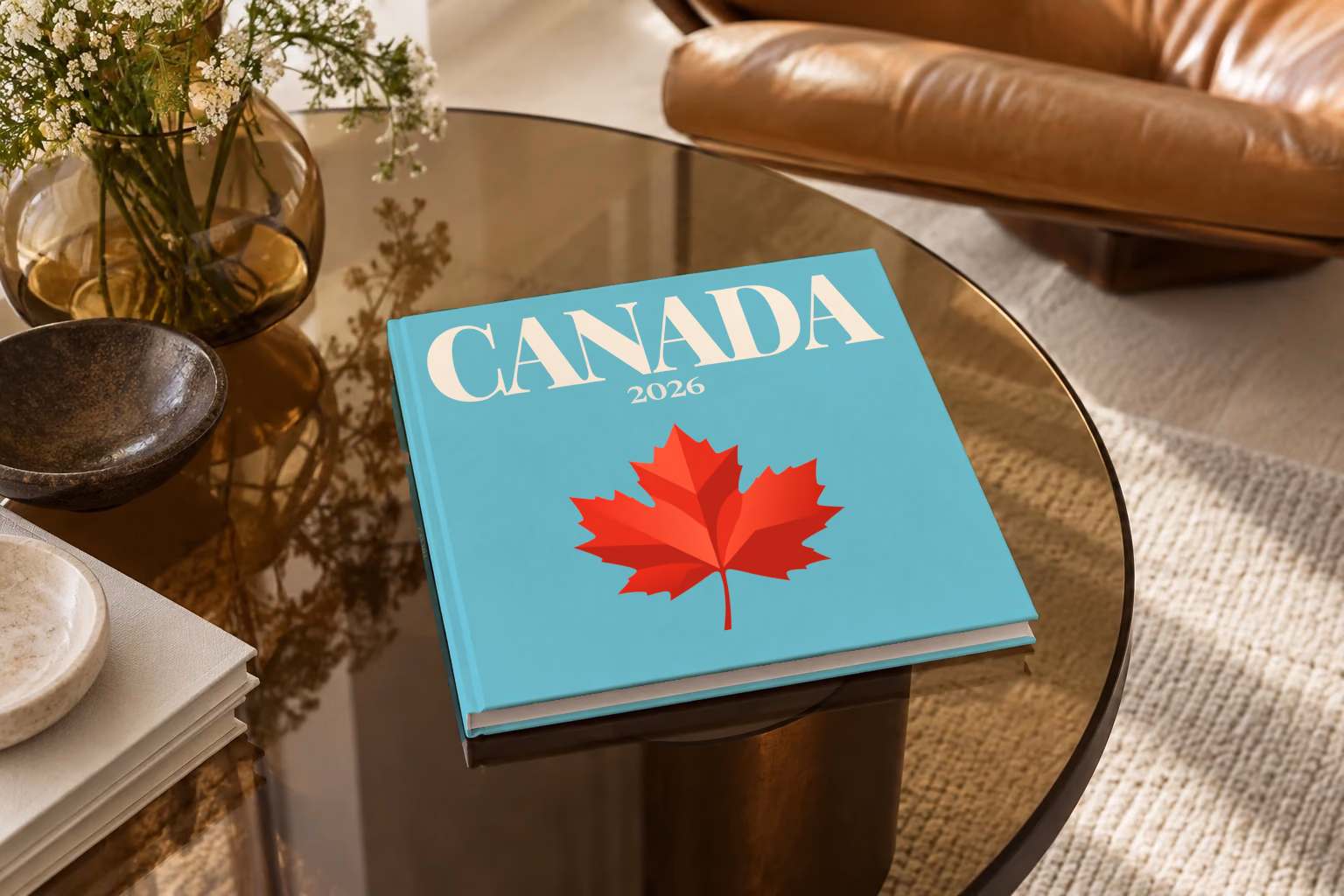 Canada square hardcover photo book with the illustrated cover of a red maple leaf on turquoise, on a smoked glass coffee table beside a leather armchair in warm afternoon light