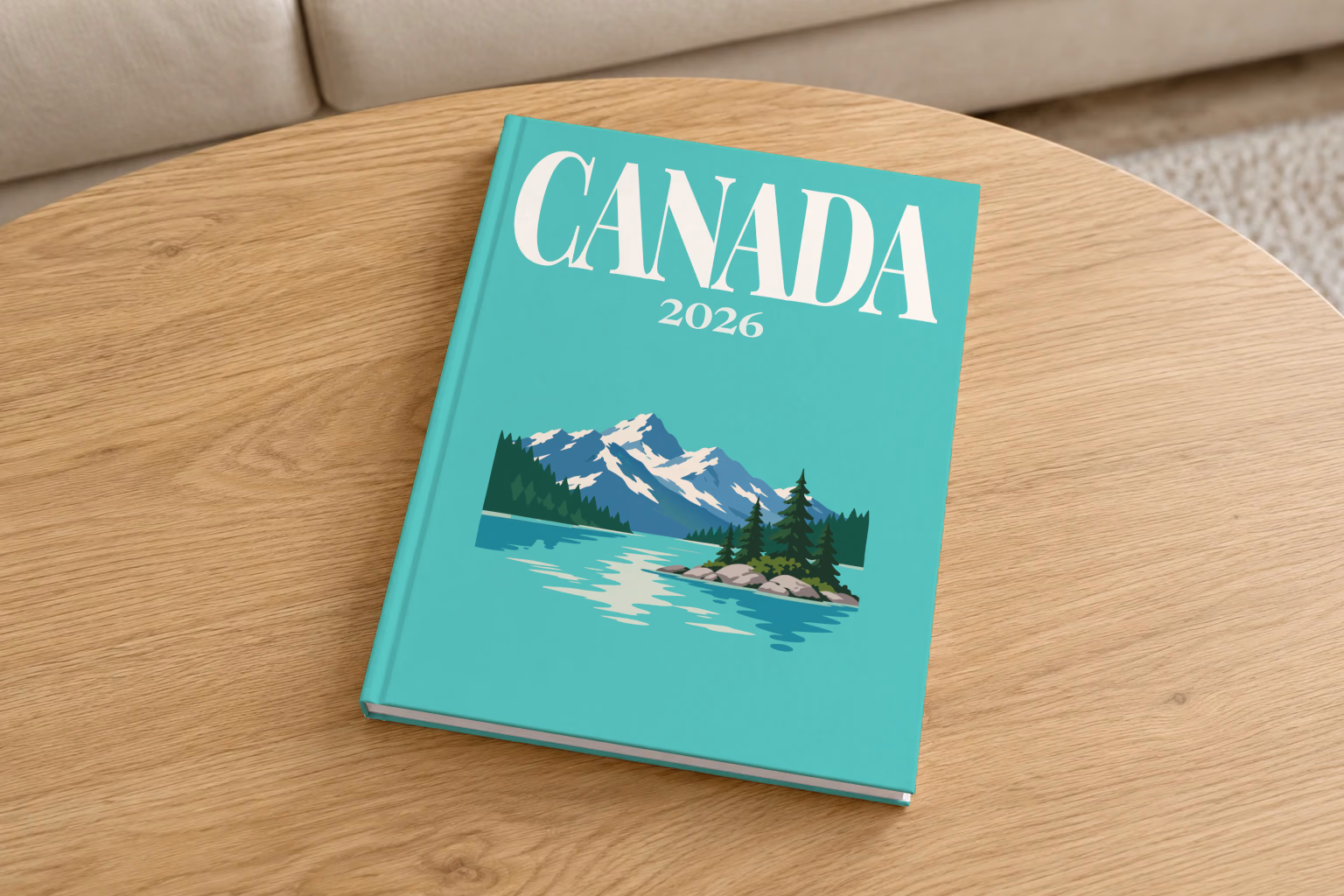 Canada hardcover photo book with the illustrated cover of a mountain lake with a pine-covered islet on mint green, on a round oak coffee table in a bright living room