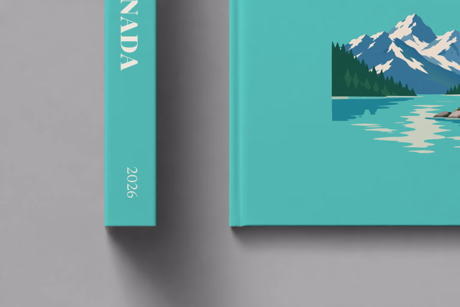 Canada hardcover photo book with the illustrated cover of a mountain lake with a pine-covered islet on mint green, shown close up beside its spine on a pale grey studio surface