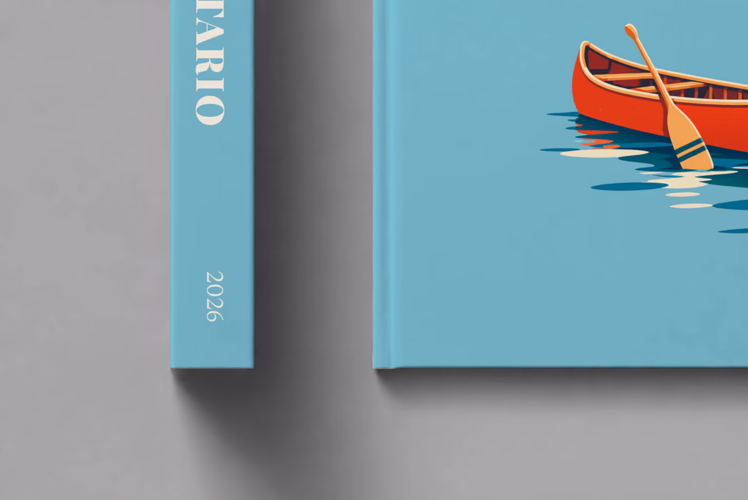 Canada hardcover photo book with the Ontario illustrated cover of a red canoe on a lake on dusty blue, shown close up beside its spine on a pale grey studio surface