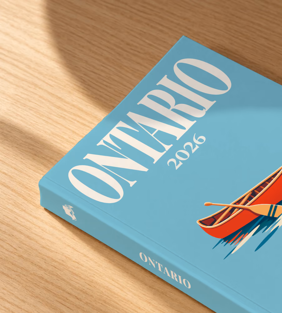 Canada softcover photo book with the Ontario illustrated cover of a red canoe on a lake on dusty blue, lying on an oak desk in dappled afternoon sunlight