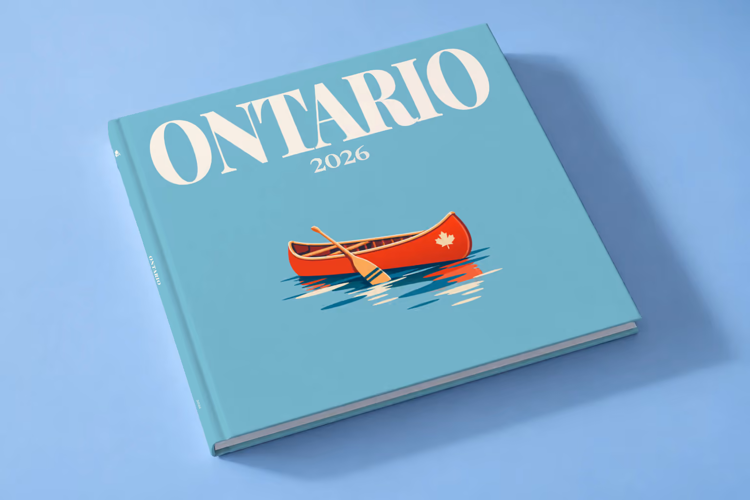 Canada square hardcover photo book with the Ontario illustrated cover of a red canoe on a lake on dusty blue, lying on a pale blue studio backdrop