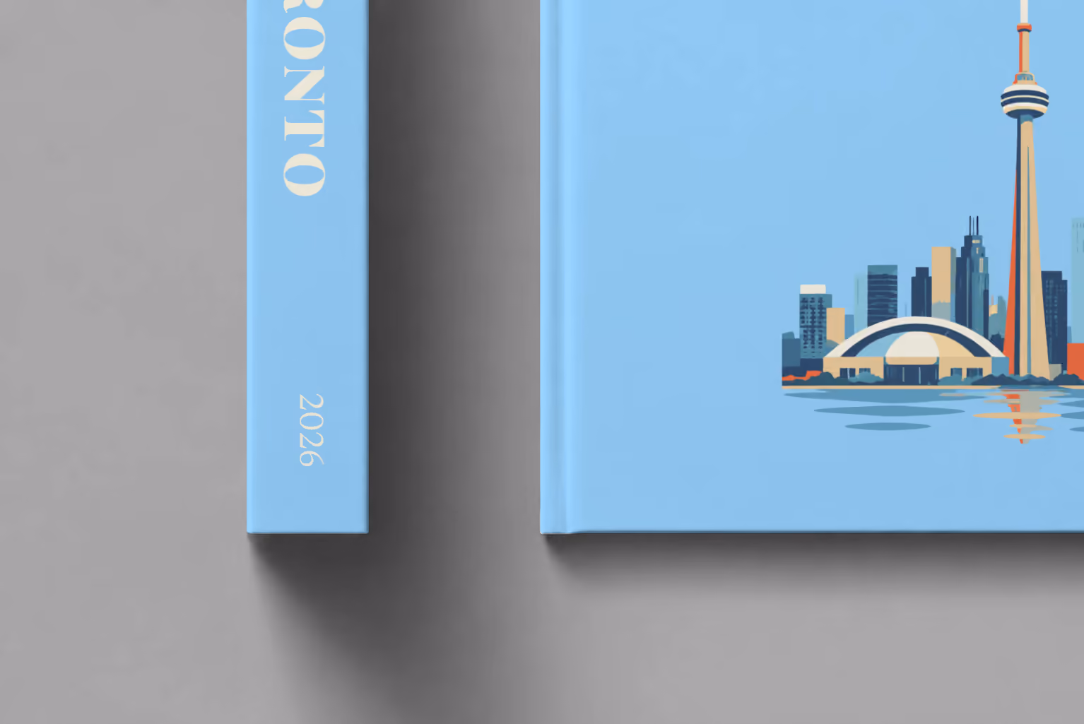 Canada hardcover photo book with the Toronto illustrated cover of the Toronto skyline and CN Tower on pale blue, shown close up beside its spine on a pale grey studio surface
