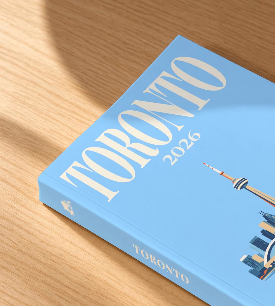 Canada softcover photo book with the Toronto illustrated cover of the Toronto skyline and CN Tower on pale blue, lying on an oak desk in dappled afternoon sunlight