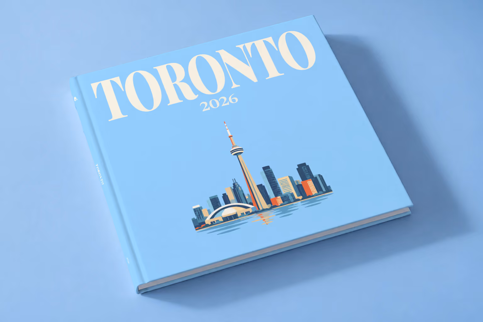 Canada square hardcover photo book with the Toronto illustrated cover of the Toronto skyline and CN Tower on pale blue, lying on a pale blue studio backdrop
