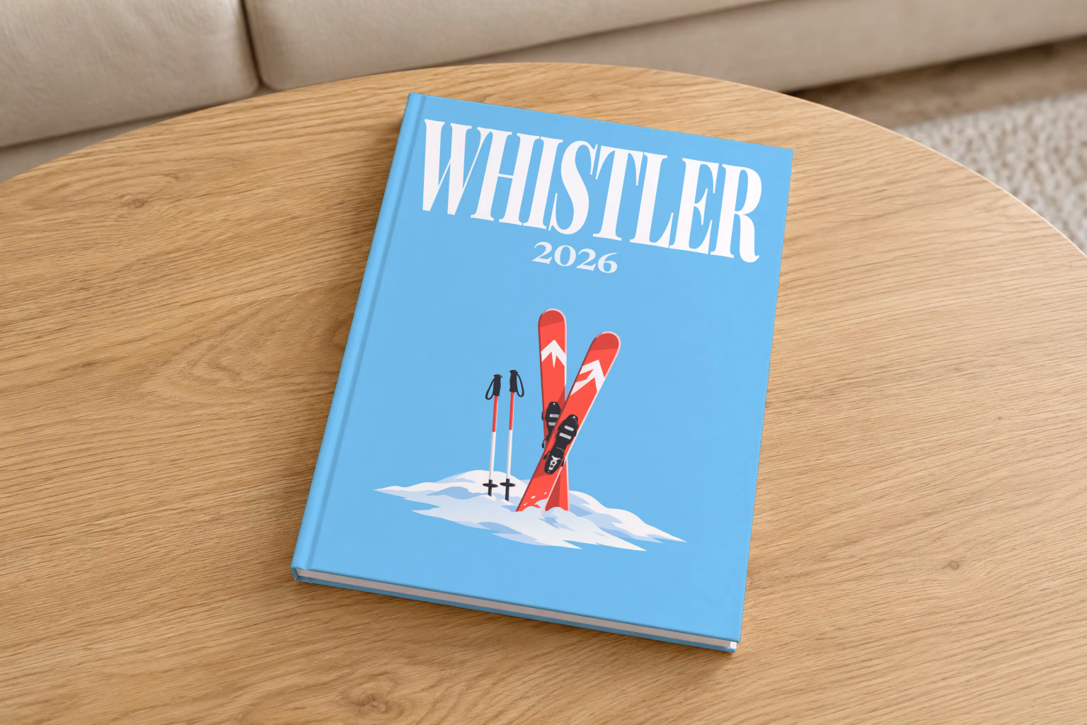 Canada hardcover photo book with the Whistler illustrated cover of red skis and poles in snow on sky blue, on a round oak coffee table in a bright living room