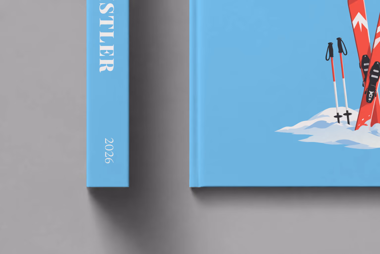 Canada hardcover photo book with the Whistler illustrated cover of red skis and poles in snow on sky blue, shown close up beside its spine on a pale grey studio surface