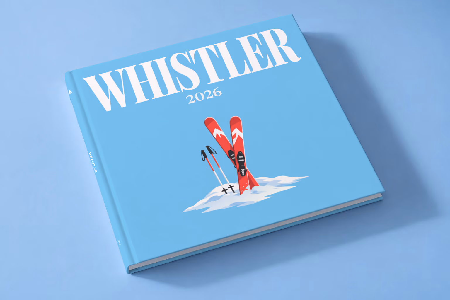 Canada square hardcover photo book with the Whistler illustrated cover of red skis and poles in snow on sky blue, lying on a pale blue studio backdrop