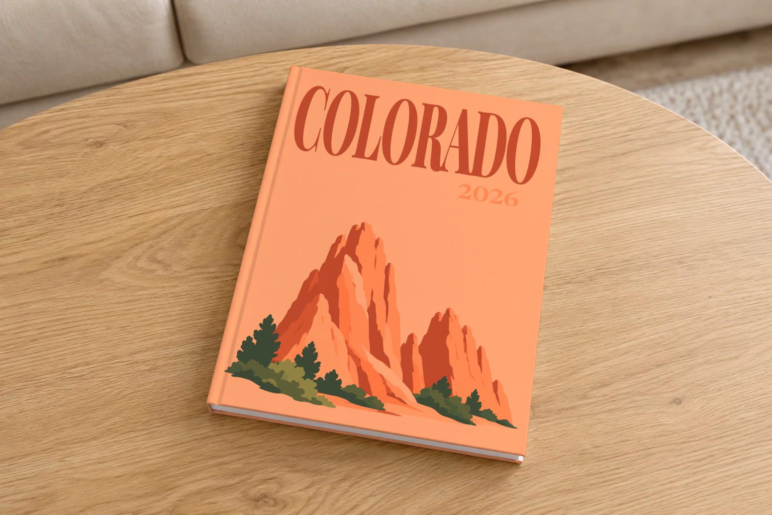 Colorado hardcover photo book with the illustrated cover of the red rock formations of Garden of the Gods on peach, on a round oak coffee table in a bright living room