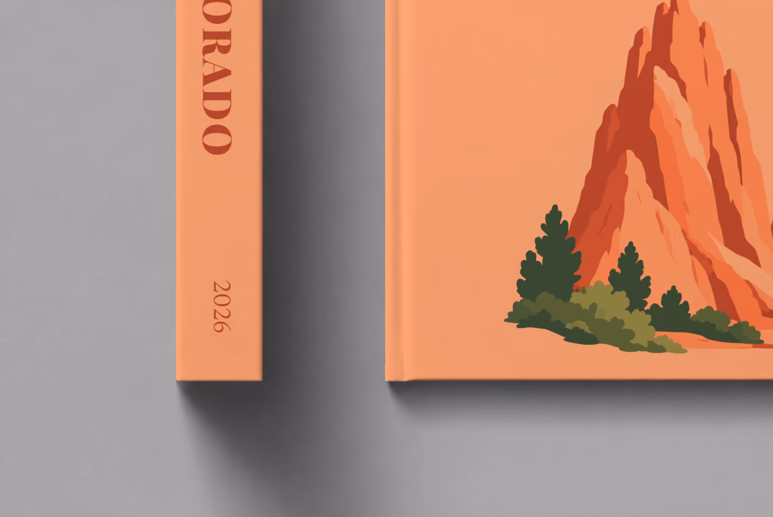 Colorado hardcover photo book with the illustrated cover of the red rock formations of Garden of the Gods on peach, shown close up beside its spine on a pale grey studio surface