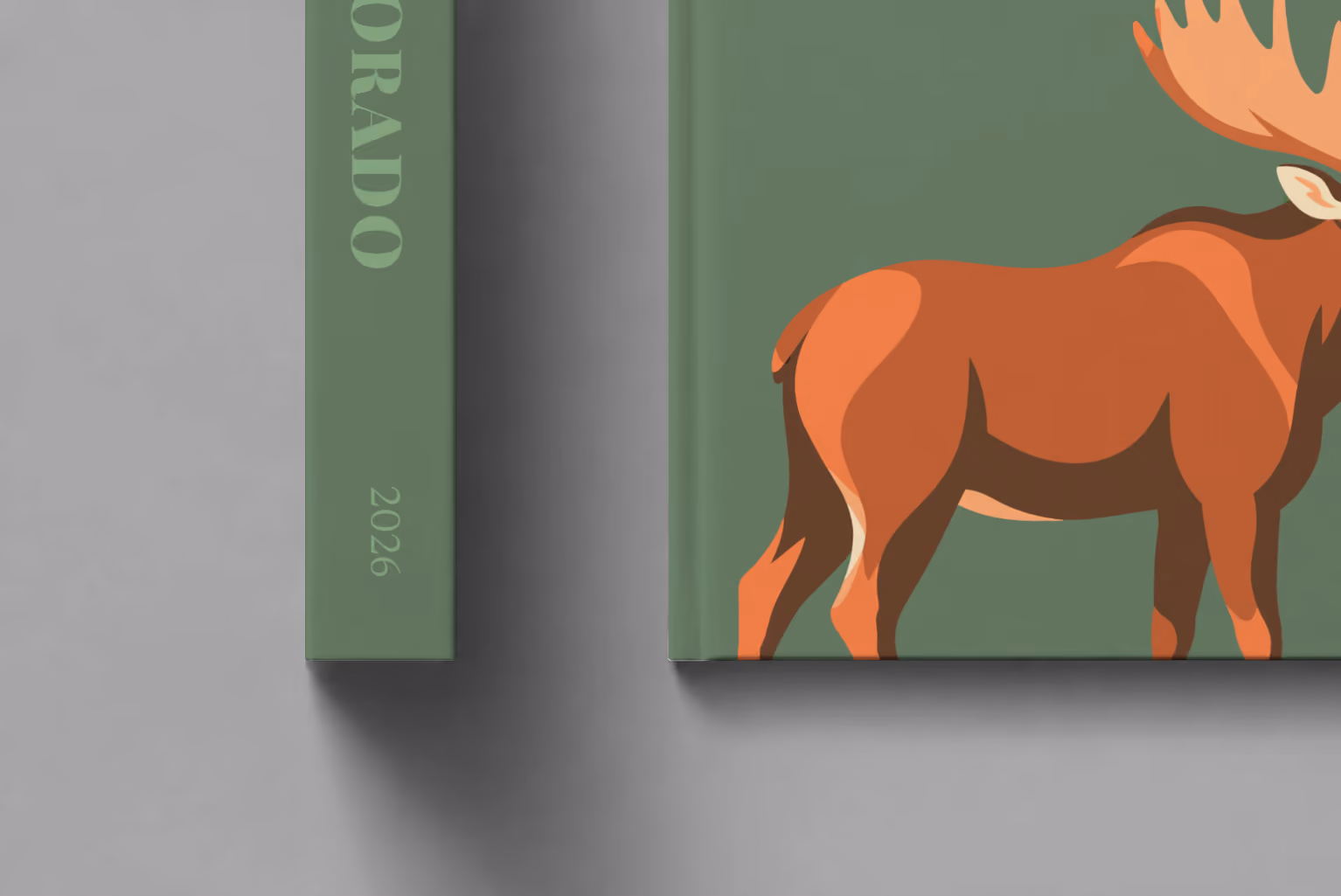 Colorado hardcover photo book with the illustrated cover of a bull moose on sage green, shown close up beside its spine on a pale grey studio surface