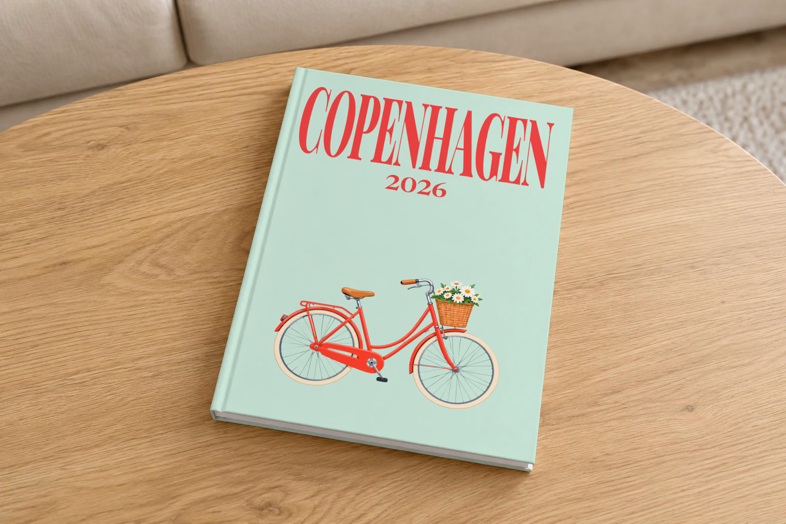 Denmark hardcover photo book with the Copenhagen illustrated cover of a red Copenhagen bicycle with a basket of daisies on mint green, on a round oak coffee table in a bright living room