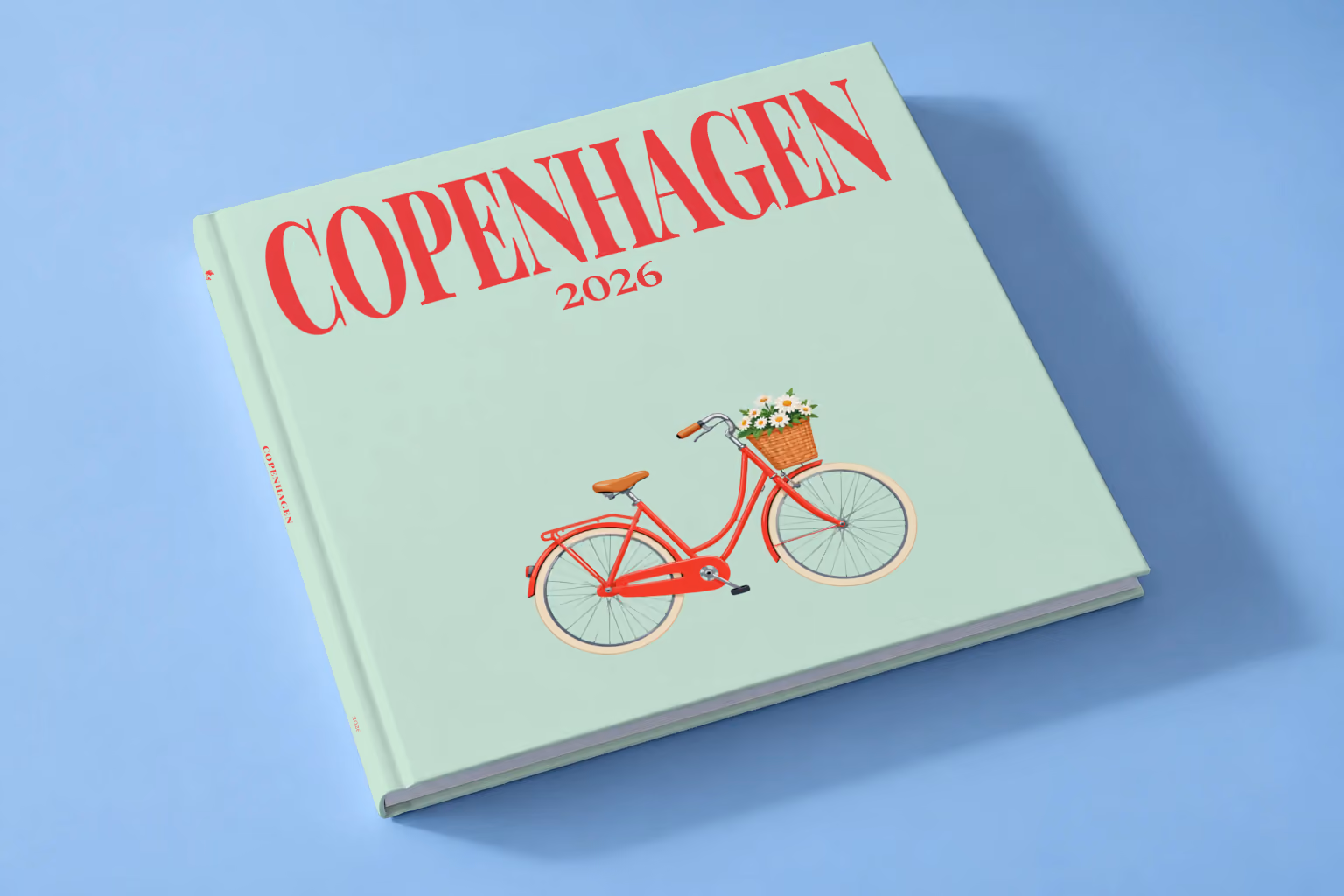 Denmark square hardcover photo book with the Copenhagen illustrated cover of a red Copenhagen bicycle with a basket of daisies on mint green, lying on a pale blue studio backdrop