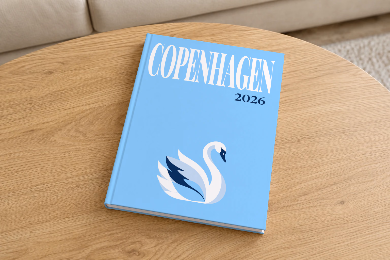 Denmark hardcover photo book with the Copenhagen illustrated cover of a white swan on sky blue, on a round oak coffee table in a bright living room
