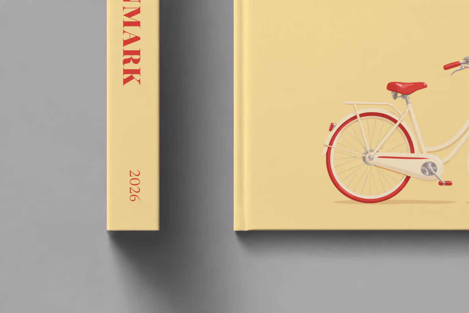 Denmark hardcover photo book with the illustrated cover of a Danish bicycle with a basket of red tulips on pale yellow, shown close up beside its spine on a pale grey studio surface