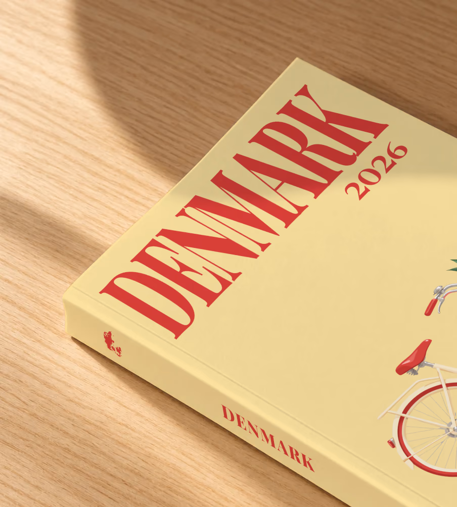 Denmark softcover photo book with the illustrated cover of a Danish bicycle with a basket of red tulips on pale yellow, lying on an oak desk in dappled afternoon sunlight