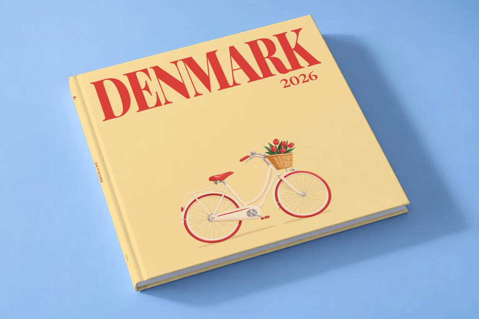 Denmark square hardcover photo book with the illustrated cover of a Danish bicycle with a basket of red tulips on pale yellow, lying on a pale blue studio backdrop