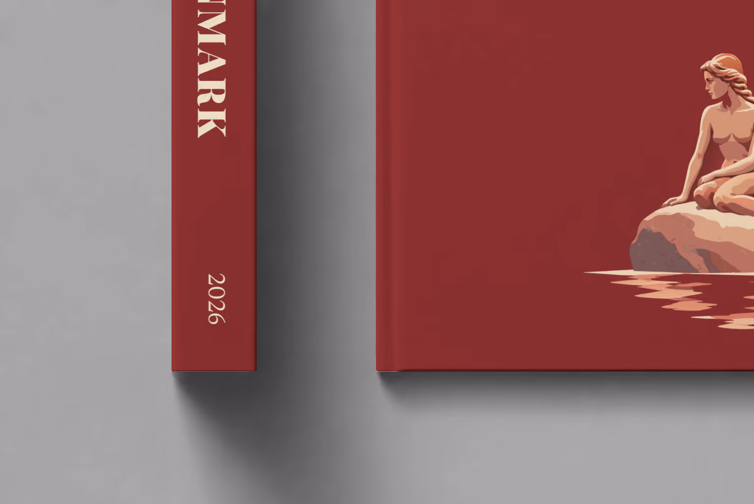 Denmark hardcover photo book with the illustrated cover of the Little Mermaid statue on her rock in Copenhagen on burgundy, shown close up beside its spine on a pale grey studio surface