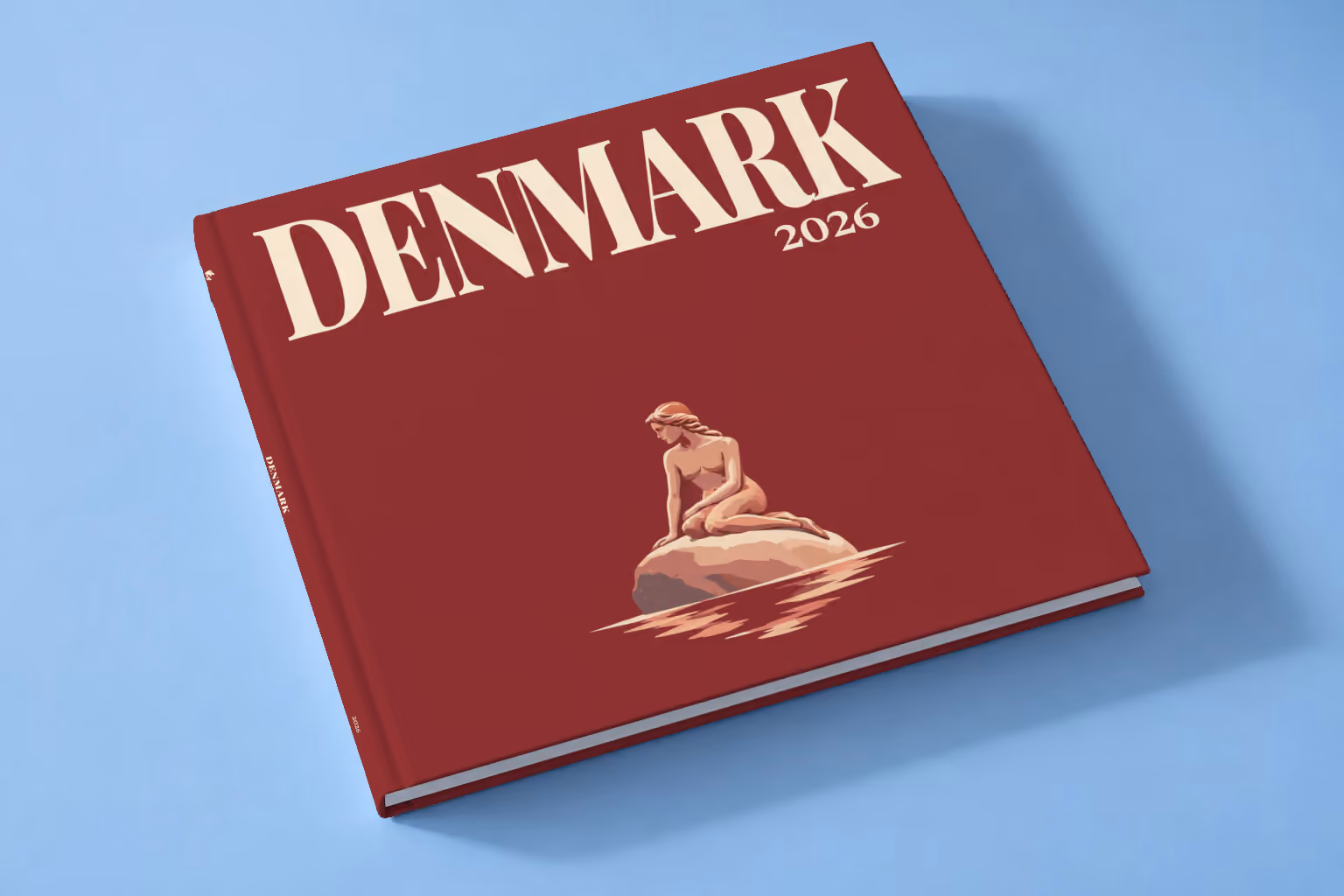 Denmark square hardcover photo book with the illustrated cover of the Little Mermaid statue on her rock in Copenhagen on burgundy, lying on a pale blue studio backdrop
