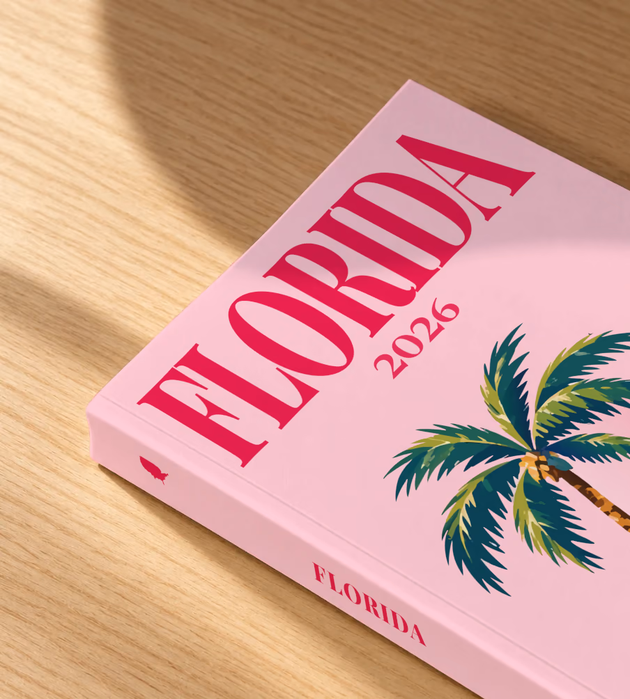Florida softcover photo book with the illustrated cover of Florida palm trees on pink, lying on an oak desk in dappled afternoon sunlight