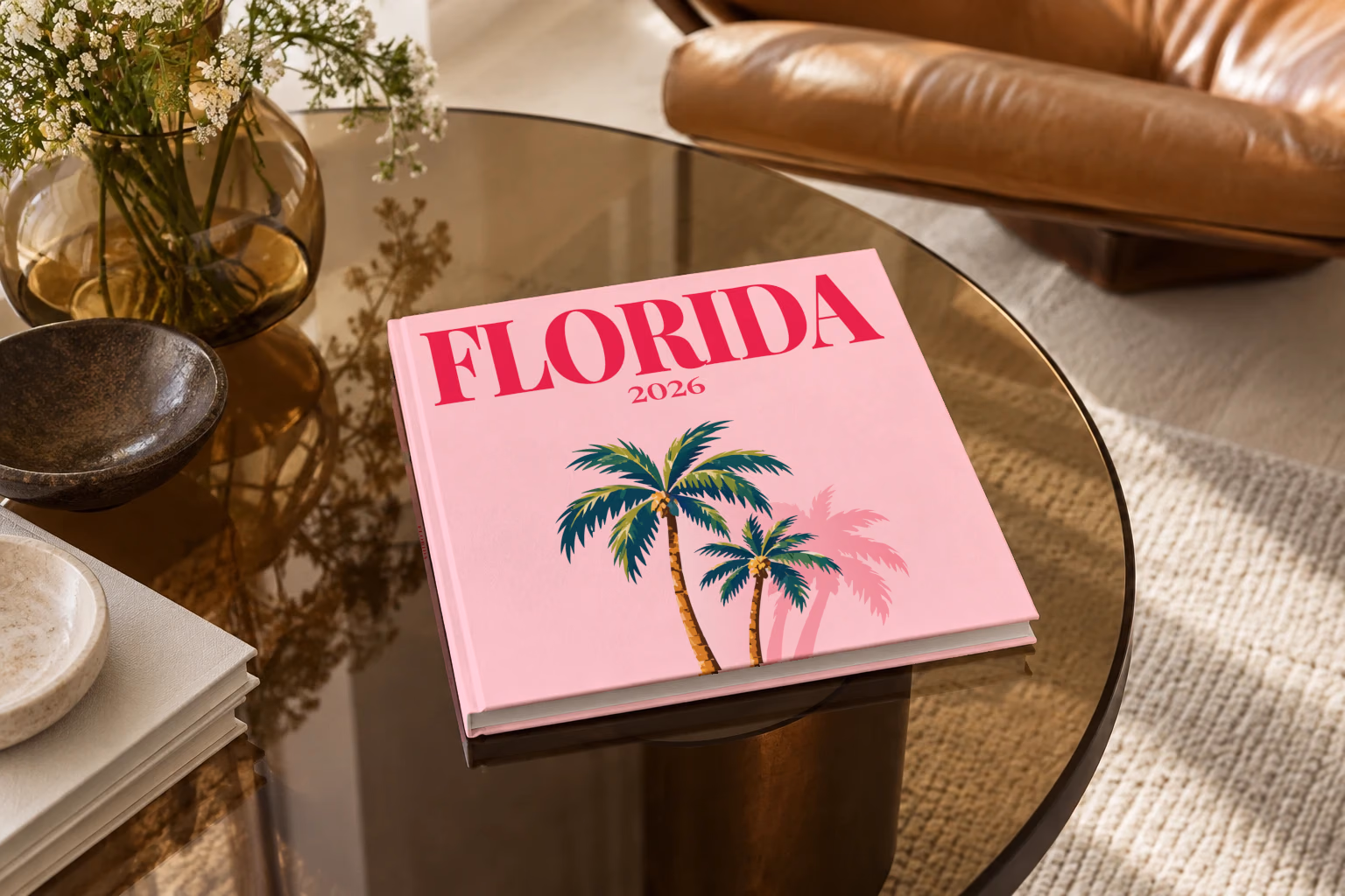 Florida square hardcover photo book with the illustrated cover of Florida palm trees on pink, on a smoked glass coffee table beside a leather armchair in warm afternoon light