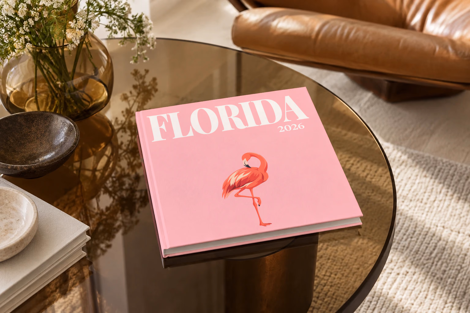 Florida square hardcover photo book with the illustrated cover of a pink flamingo on pink, on a smoked glass coffee table beside a leather armchair in warm afternoon light