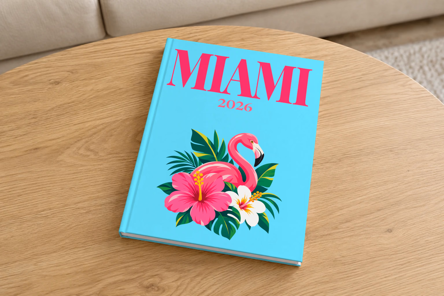 Florida hardcover photo book with the Miami illustrated cover of a pink flamingo with hibiscus flowers and palm leaves on aqua, on a round oak coffee table in a bright living room