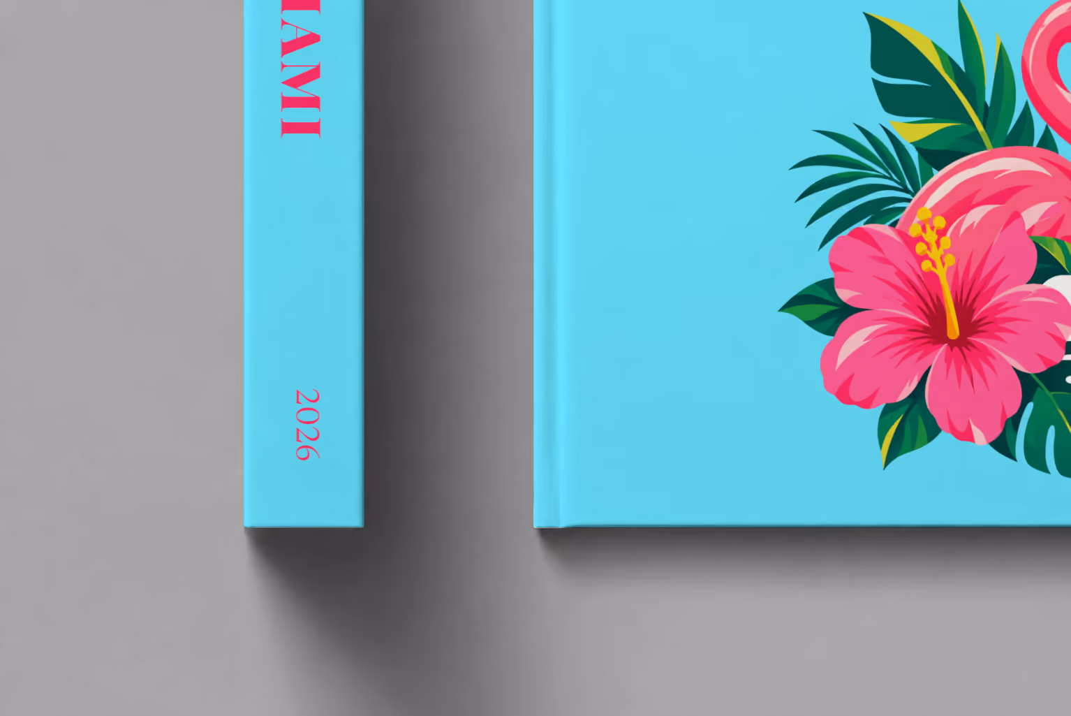 Florida hardcover photo book with the Miami illustrated cover of a pink flamingo with hibiscus flowers and palm leaves on aqua, shown close up beside its spine on a pale grey studio surface