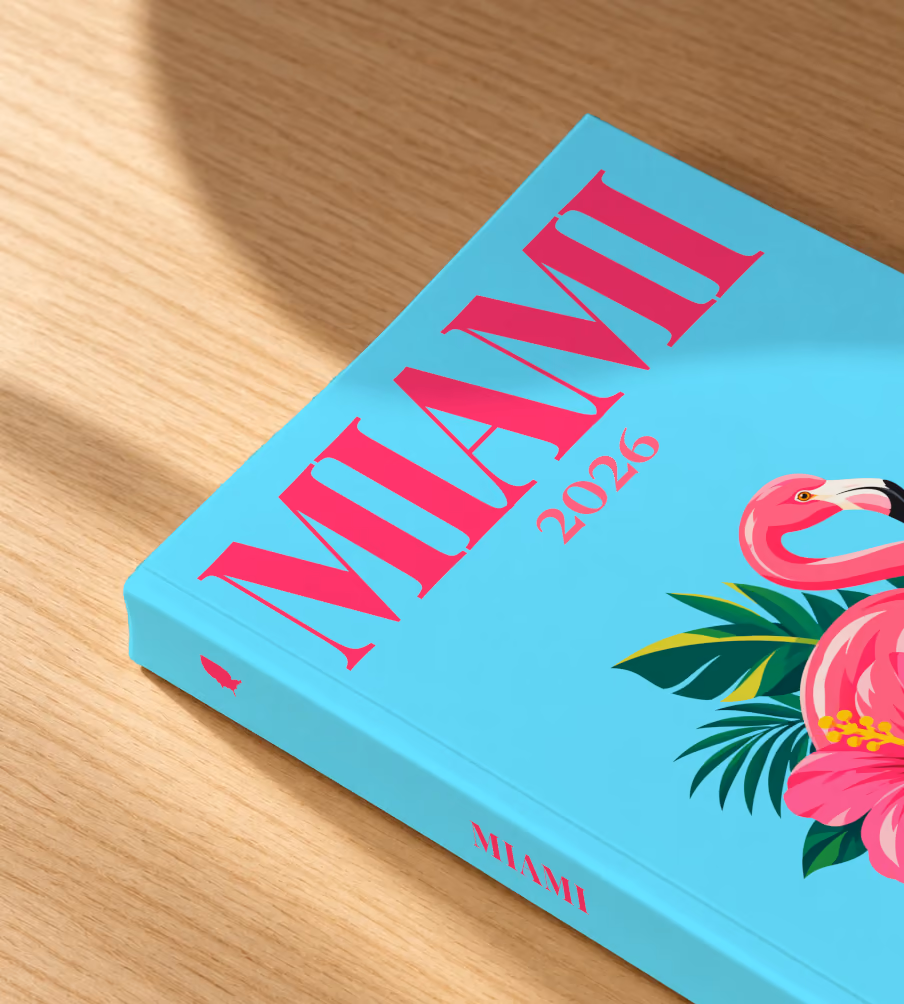 Florida softcover photo book with the Miami illustrated cover of a pink flamingo with hibiscus flowers and palm leaves on aqua, lying on an oak desk in dappled afternoon sunlight