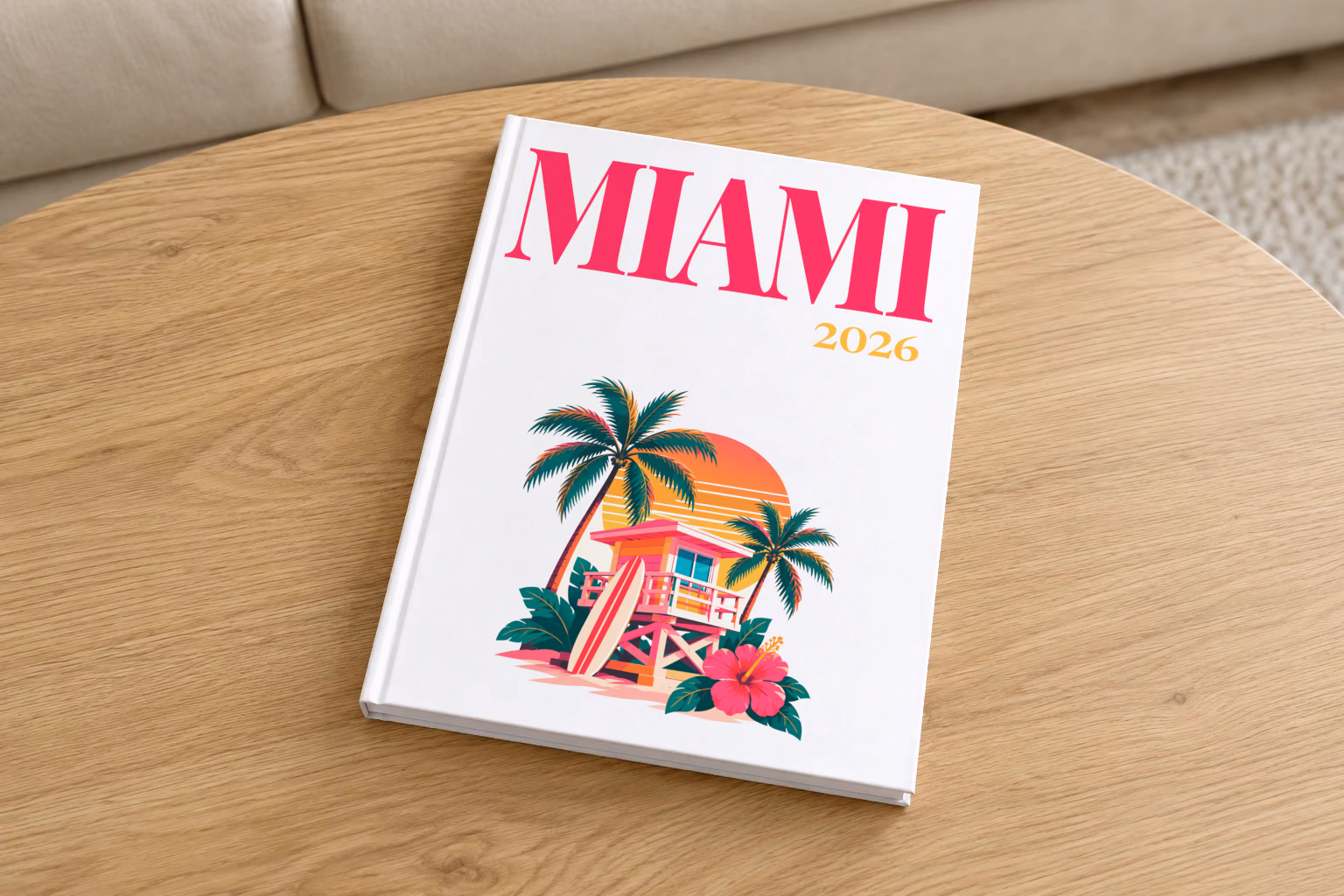 Florida hardcover photo book with the Miami illustrated cover of a pink Miami Beach lifeguard tower with palm trees at sunset on white, on a round oak coffee table in a bright living room
