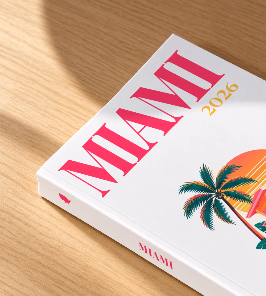Florida softcover photo book with the Miami illustrated cover of a pink Miami Beach lifeguard tower with palm trees at sunset on white, lying on an oak desk in dappled afternoon sunlight