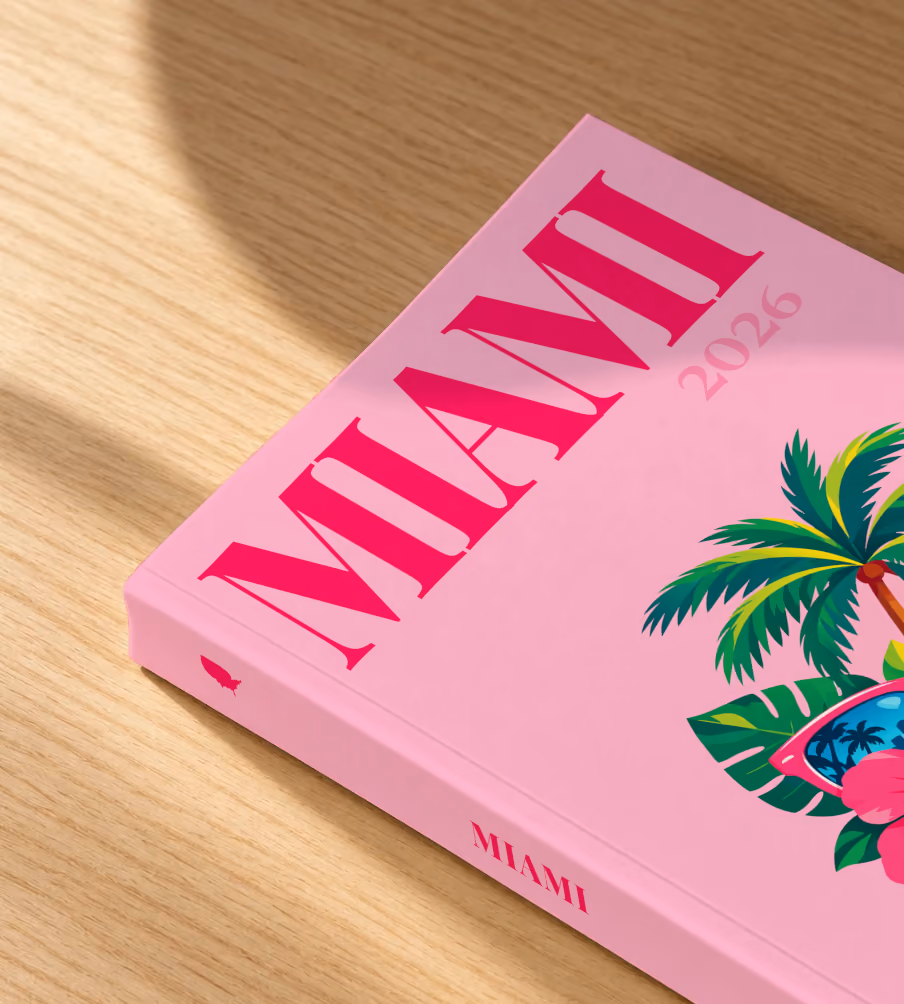 Florida softcover photo book with the Miami illustrated cover of pink sunglasses reflecting palm trees, with hibiscus, on pink, lying on an oak desk in dappled afternoon sunlight