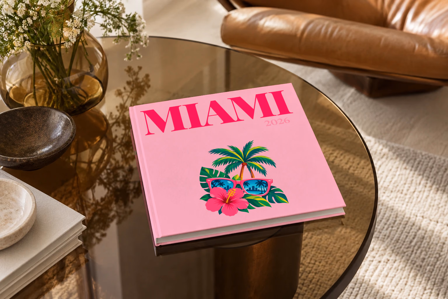 Florida square hardcover photo book with the Miami illustrated cover of pink sunglasses reflecting palm trees, with hibiscus, on pink, on a smoked glass coffee table beside a leather armchair in warm afternoon light